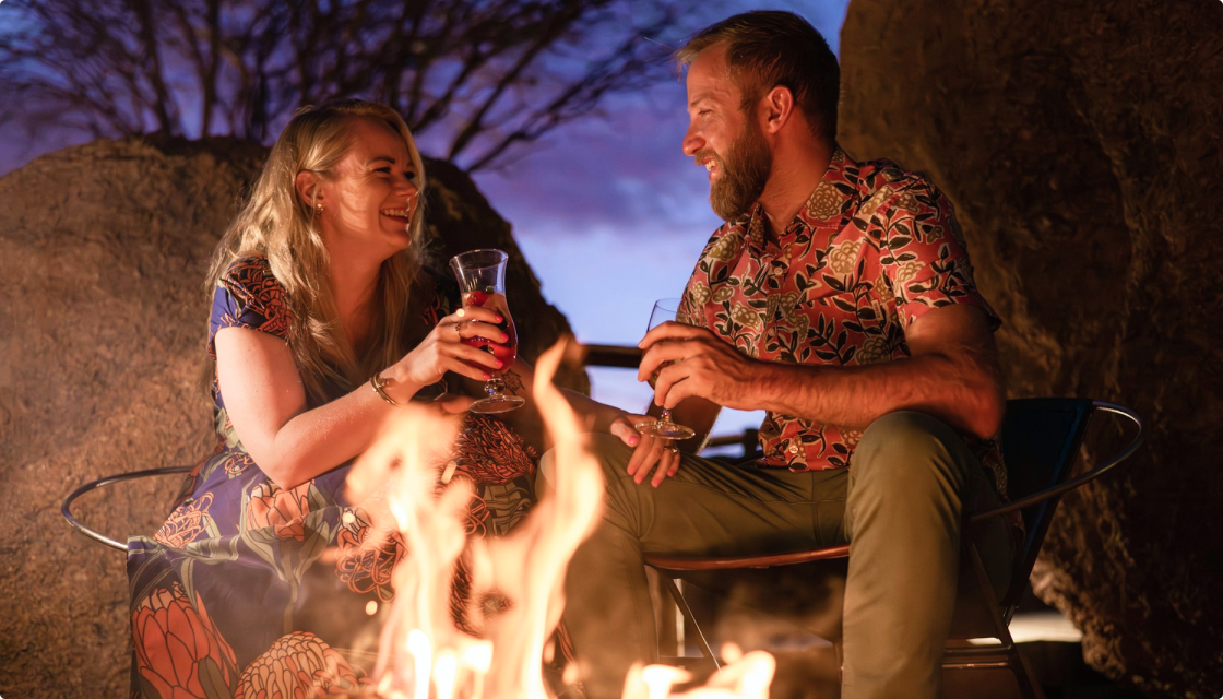 Enamel mug with vodka cocktail by a glowing campfire under starry summer skies